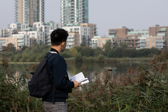 A young adult looking out at water in front of a London city scape. 