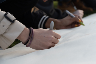 A close up image of two hands, two young adults using pens to draw on a large piece of paper.