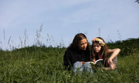 A woman and girl reading on a grass bank