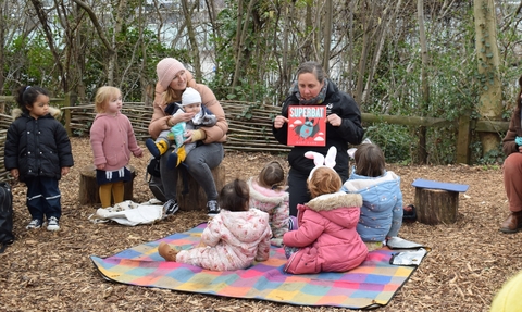 Group of children listening to a story seated on a blanket in a woodland environment