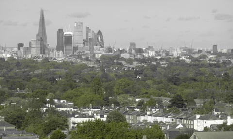 A skyline view of the city of London, tall sky scrapers are in the background with a expanse of trees below dotted with buildings