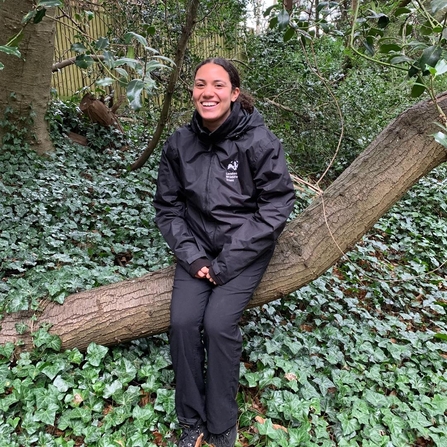 Keeping it Wild trainee Yasmin leaning against a tree in a woodland, smiling.