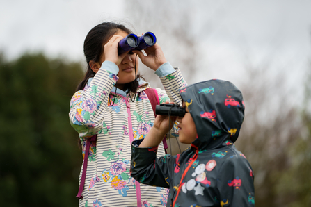 two children stand looking through binoculars