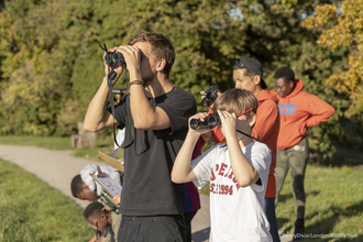 A group of children and an adult with binoculars looking out into the distance
