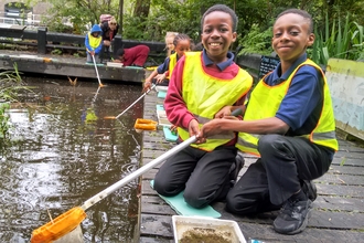 Two school children smiling whilst pond dipping at Camley Street Natural Park