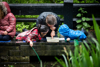 Two children and an adult pond dipping in the rain. The adult is pointing at something in a white tray