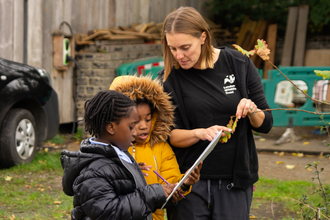 Two children look intently at a clipboard they are holding next to a teacher looking overhead 