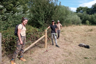 Three volunteers stand next to fencing they have just built