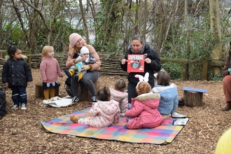 Group of children listening to a story seated on a blanket in a woodland environment