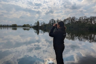 Yasmin, a young adult using binoculars to look out at birds on the water at Walthamstow wetlands.