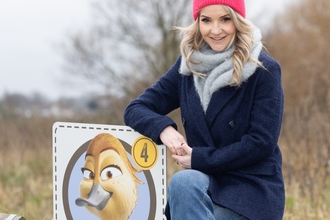 Presenter Helen Skelton sat on a fence with a Migration Trail point at Walthamstow Wetlands