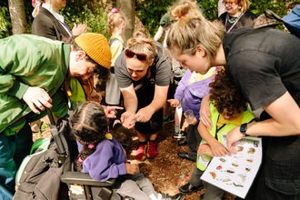 A group of individuals gathered around a child in a wheelchair, looking at a mini beast in someone's hand