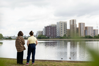 Two people looking out at the water at Walthamstow Wetlands with city buildings in the distance.