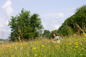 A young woman sitting smiling in a grassy meadow filled with wildflowers
