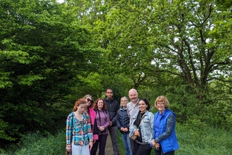 A group of 8 people standing in the clearing of a woodland in summer