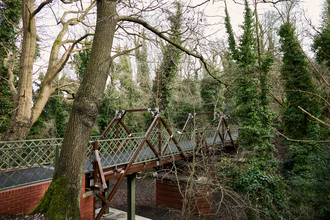 A restored metal footbridge with green lattice railings in a wooded area.