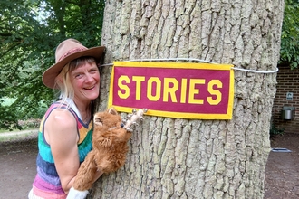 Woman stood next to a tree holding a fox puppet pointing at a stories sign