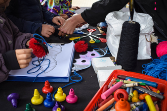 A table full of art and craft supplies, several pairs of hands are in view making bat crafts
