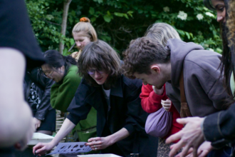 A group of young people gathered around a pond looking in to it 