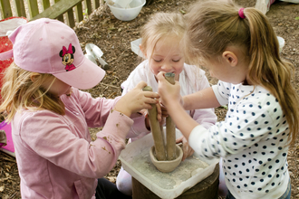 Three children use a pestle and mortar to mix paint