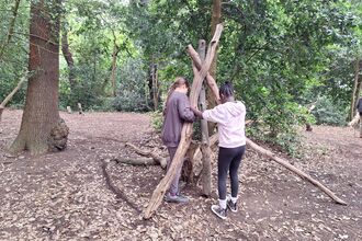 Two young people building a mini shelter using branches in the woodland