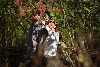 Two people look up into a canopy of trees as they are surrounded by foliage.