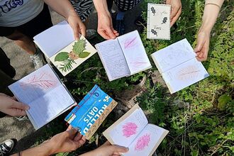 Hands holding hand made books with items from nature in them over a patch a grass