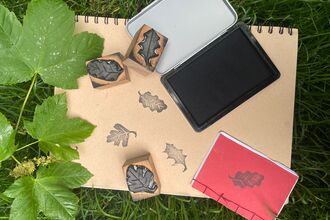 A book with oak stamps in black ink, with the wooden stamps on top, and a few leaves.