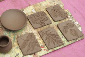 A collection of handcrafted pottery and leaf impression clay tiles on a textured surface.