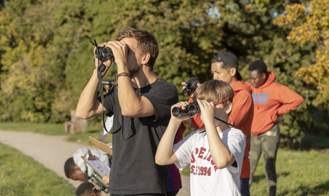 A group of children and an adult with binoculars looking out into the distance
