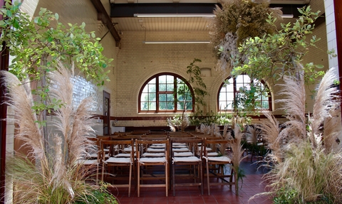 A building in Walthamstow Wetlands set up for a wedding, rows of chairs sit in front of plumes of foliage decorating the ceiling and lining the floor