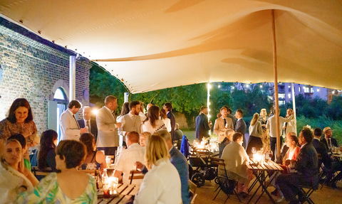 A group of people stood and sat around candle lit tables