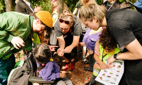 A group of individuals gathered around a child in a wheelchair, looking at a mini beast in someone's hand