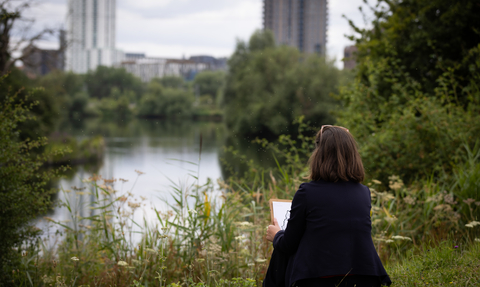 a person sat down holding a clipboard looking out at the wetlands