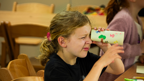 a child holding a cardboard tube holding it up to their eye and looking through it