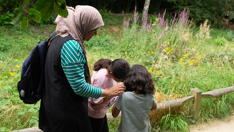 A mum with her two children standing by some greenery looking at pictures on a clipboard