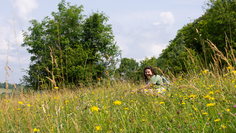 A young woman sitting smiling in a grassy meadow filled with wildflowers