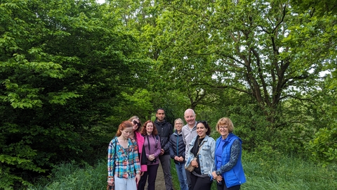 A group of 8 people standing in the clearing of a woodland in summer