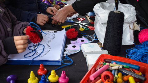 A table full of art and craft supplies, several pairs of hands are in view making bat crafts