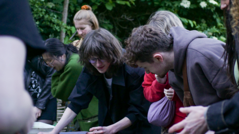 A group of young people gathered around a pond looking in to it 