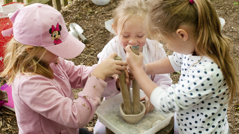 Three children use a pestle and mortar to mix paint 