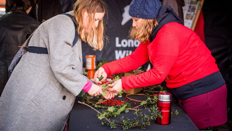 Two people standing over a table holding a festive wreath