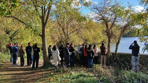 A group of people are pictured from behind using binoculars to look out across trees and a body of water