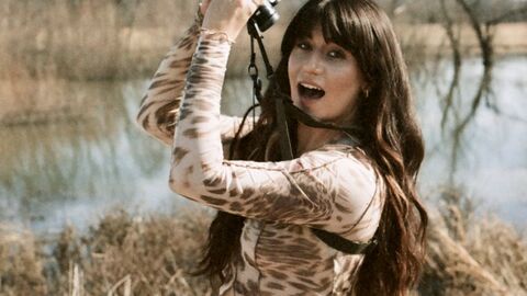 Young woman looking at camera and holding binoculars up to the sky, water and reeds behind her