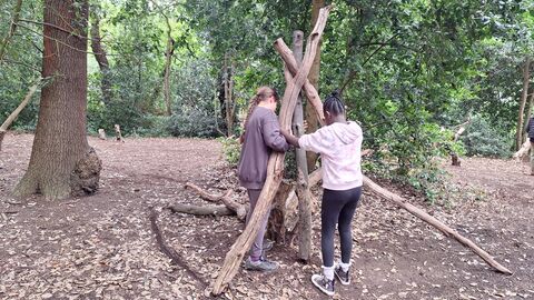 Two young people building a mini shelter using branches in the woodland