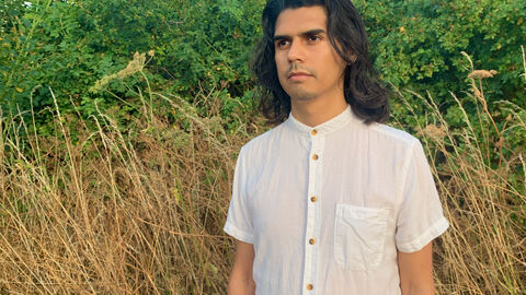 A young person looking away from the camera, in the background tall overflowered vegetation and a hedgerow
