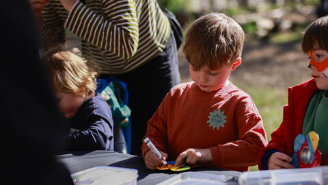 Children decorate wooden butterfly feeders on a sunny day