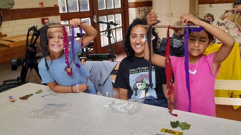 An adult and two children sit at a table and hold up some journey sticks crafts they've made