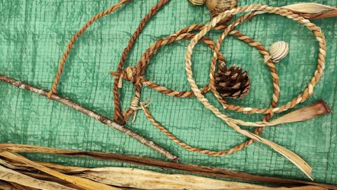 Cordage rope with a bead and pinecone attached on a green tarp.