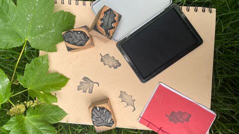 A book with oak stamps in black ink, with the wooden stamps on top, and a few leaves.